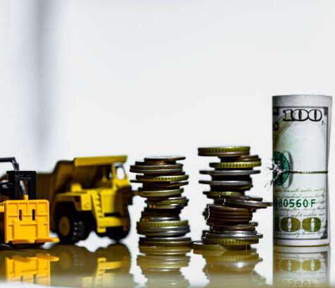 Financial And Macro Economic Concept, pile of coins money stacked on wooden table, with construction vehicle and equipment. Vintage tone.